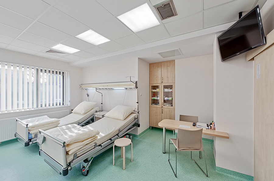 Dwuosobowa sala pacjentów z dużymi łóżkami, stolikiem i telewizorem zawieszonym przy suficie